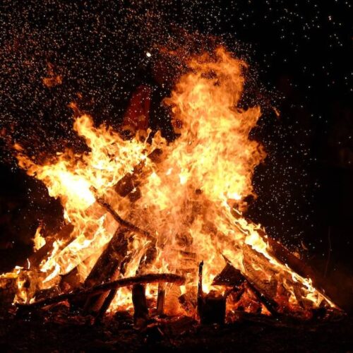 A large, crackling bonfire against a dark night background, following all bonfire safety guidelines.