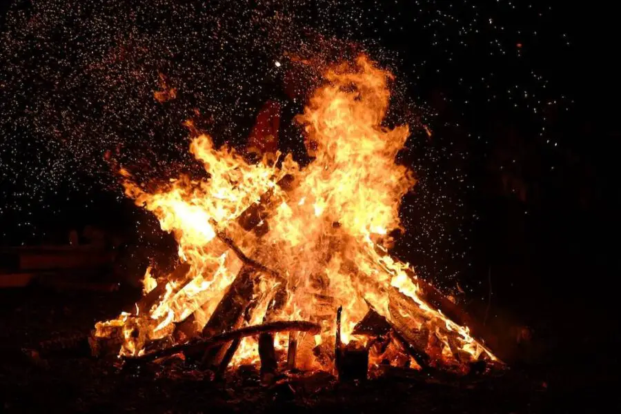 A large, crackling bonfire against a dark night background, following all bonfire safety guidelines.