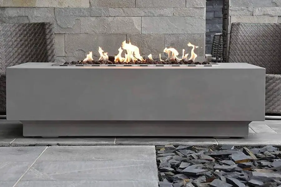 Modern outdoor gas fire pit table with flames and a built-in cost calculator, surrounded by two woven armchairs on a stone patio.