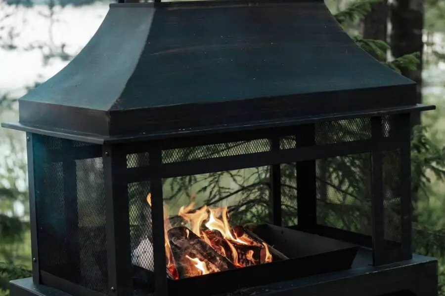 Outdoor metal safest fire pit with flames, set against a natural backdrop of trees and a lake.
