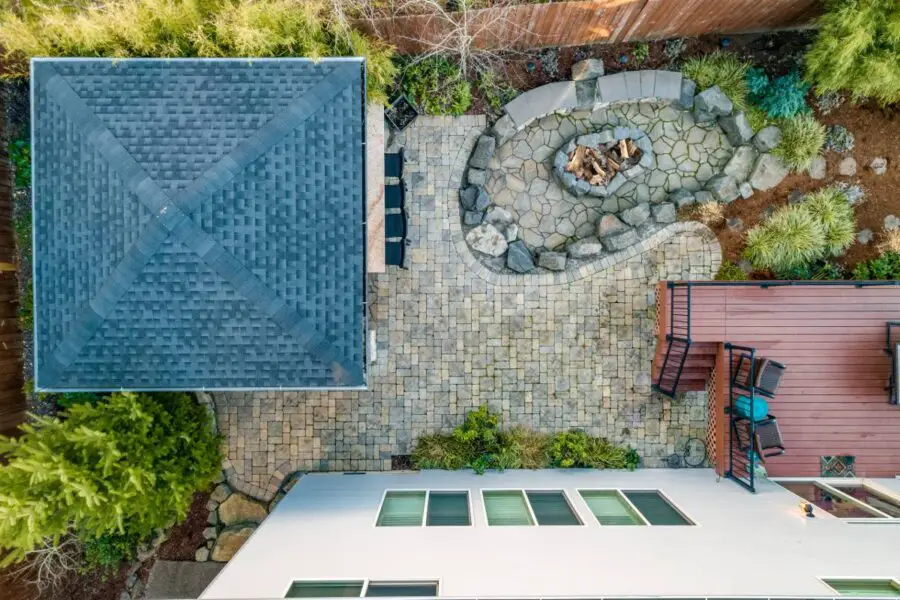 Aerial view of a backyard with a patio, distance requirements observed around the wood fire pit area, and parts of two houses visible.