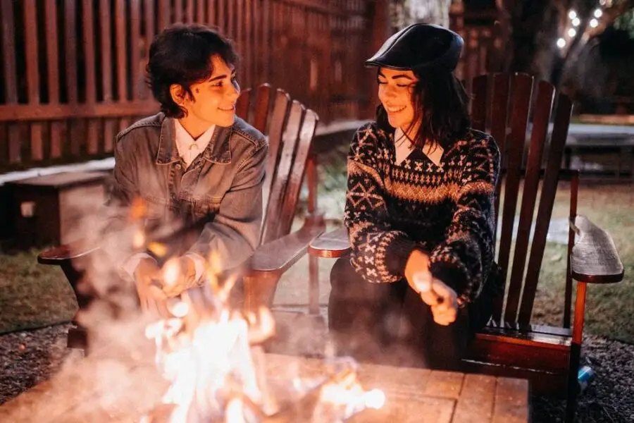 Two individuals enjoying a conversation by a fire pit, surrounded by a fence, at night.