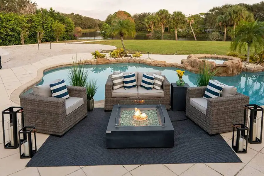 An outdoor seating area with a fire pit table, surrounded by a pool deck and landscaped garden.