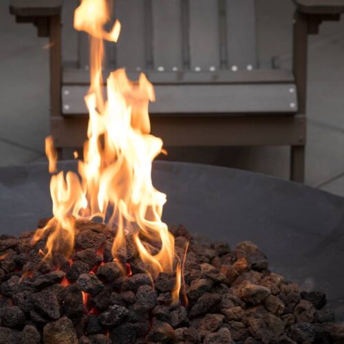 A fire pit with burning flames surrounded by Adirondack chairs is put on the driveway.