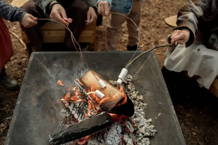 Three individuals roasting marshmallows over a fire pit.