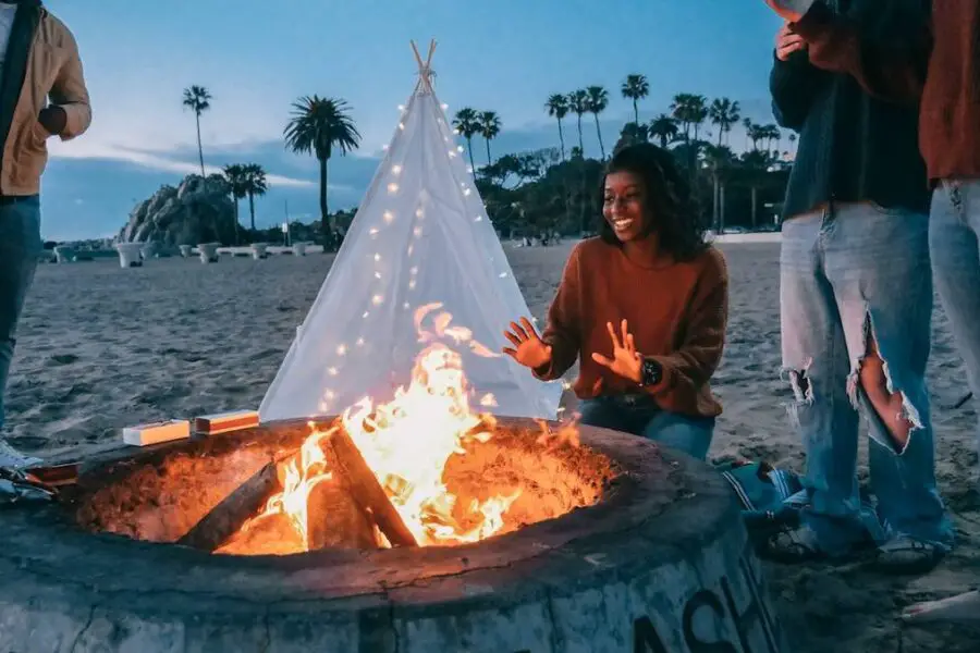 Group of friends enjoying a bonfire in a fire pit on the beach at dusk.