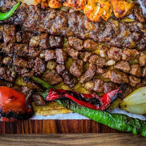 Assorted grilled meats and vegetables cooked over a fire pit and served on a wooden platter.