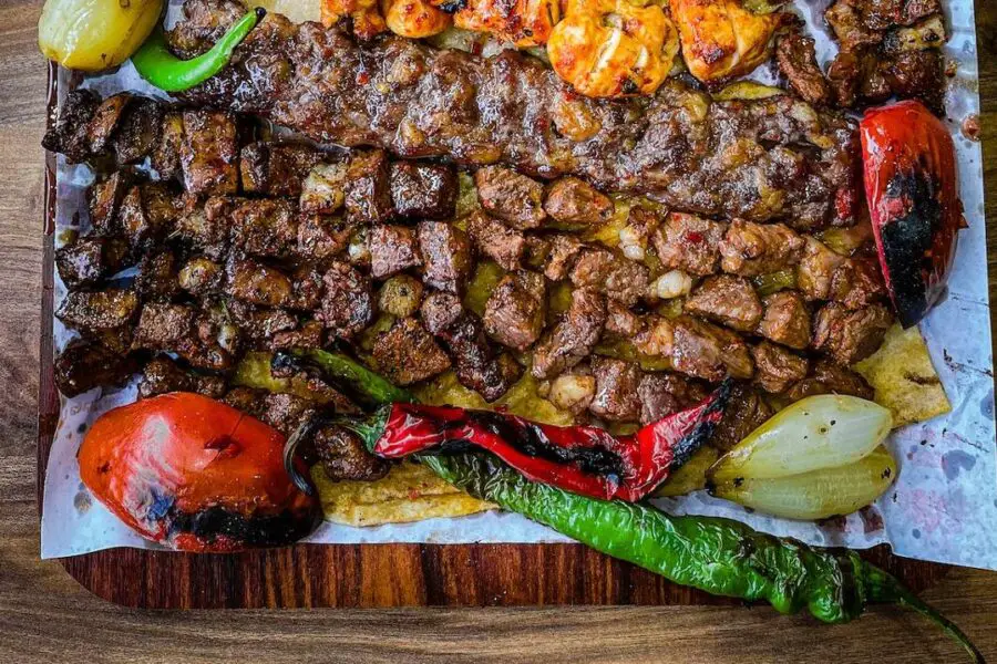 Assorted grilled meats and vegetables cooked over a fire pit and served on a wooden platter.