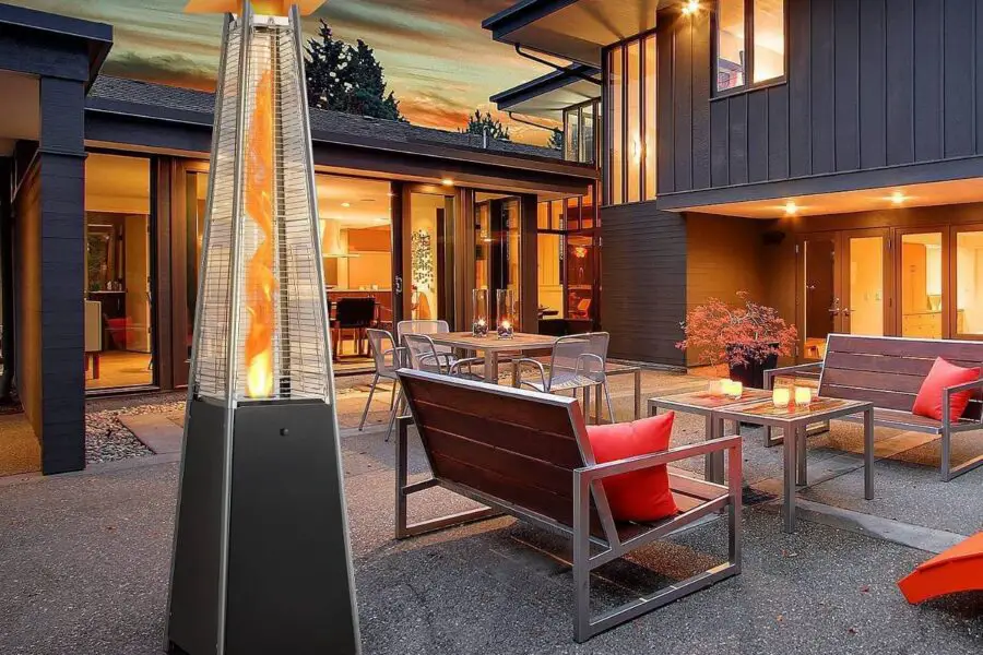 A modern outdoor patio area at dusk with a close patio heater, seating, and the interior of the house visible in the background.