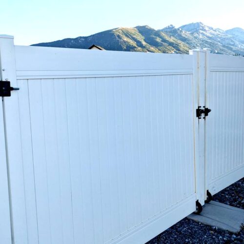 White vinyl fence with a closed gate in the foreground and a mountainous landscape in the background, designed for fire safety to resist catching on fire.