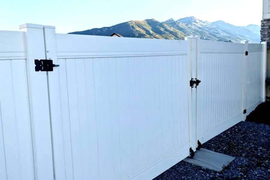 White vinyl fence with a closed gate in the foreground and a mountainous landscape in the background, designed for fire safety to resist catching on fire.