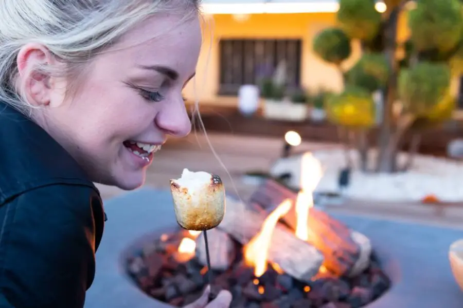Woman demonstrating fire pit safety while roasting a marshmallow over a fire pit.