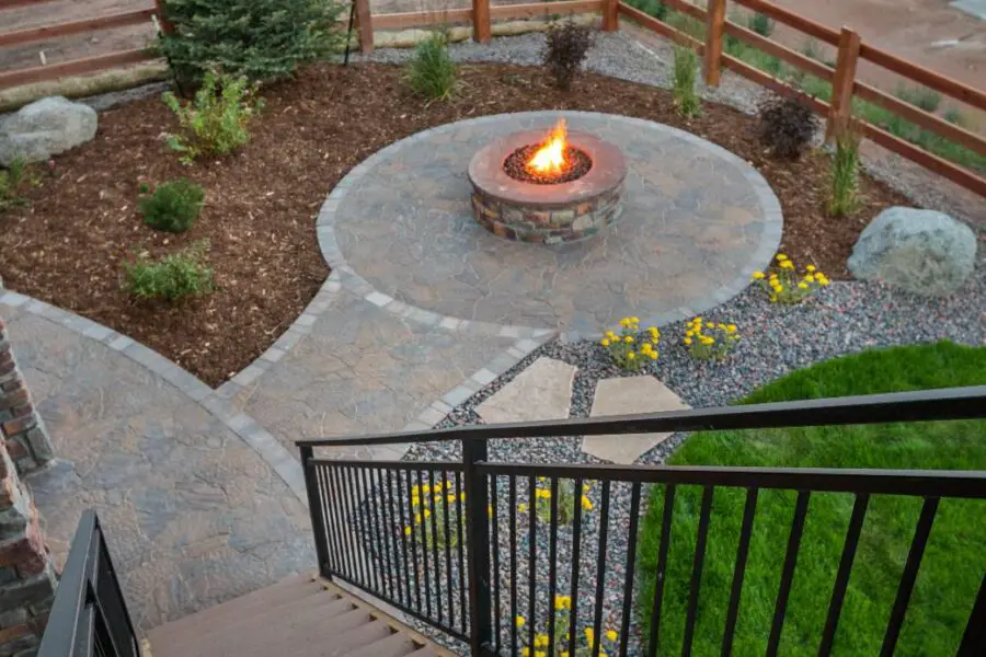 A well-maintained backyard, viewed from a deck, showcases the best place for a fire pit, surrounded by a stone path and landscaped garden.