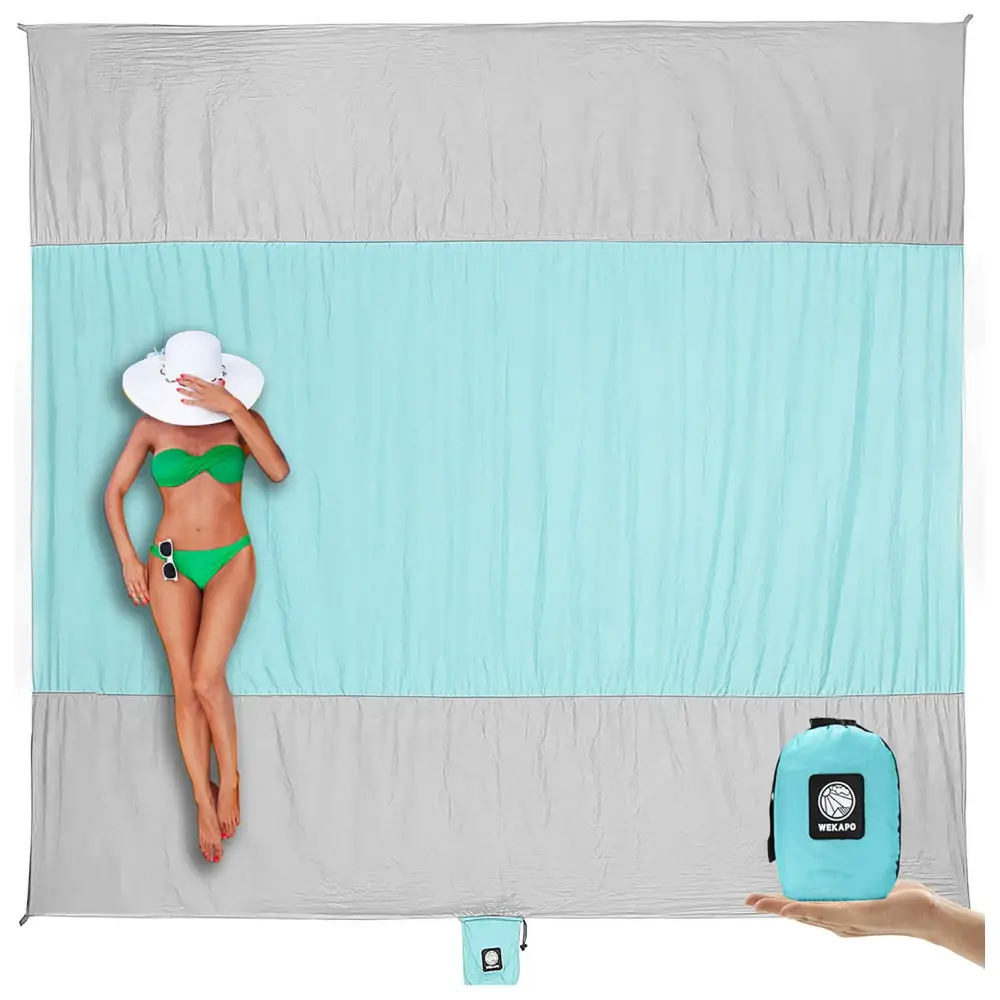 Woman in a green bikini lying on a turquoise and gray beach towel, holding a white hat over her face.