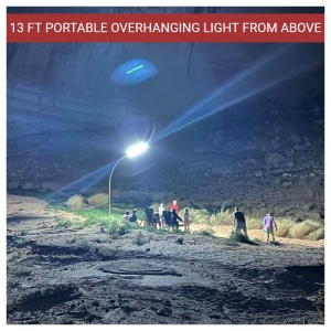A portable overhanging light illuminates a group of people gathered in a rocky area at night.