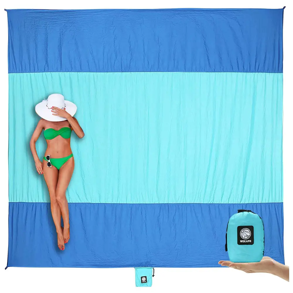 A woman in a green bikini lying on a blue oversized beach blanket with a white hat covering her face.