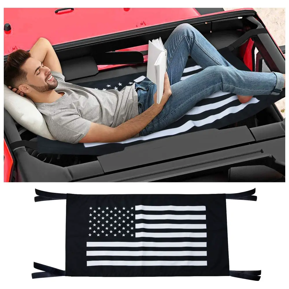 Man reclining in a hammock attached to a red vehicle, reading a book with a black and white american flag design on the hammock fabric.