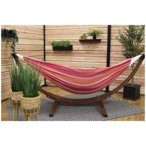 A colorful striped hammock on a wooden stand, indoors with decorative plants and woven chairs.