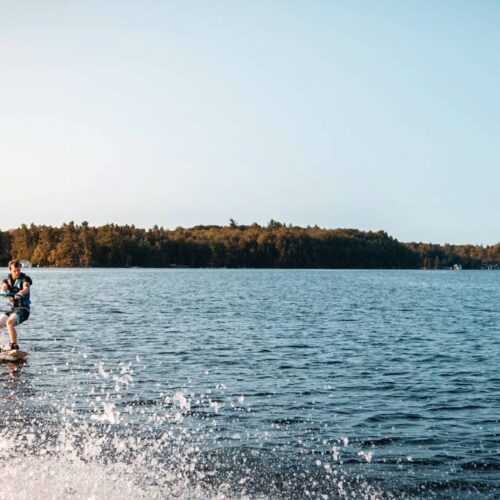 A person wakeboarding on a lake, towed by an off-frame boat using one of the best wakeboard ropes, with a forested shoreline in the background.