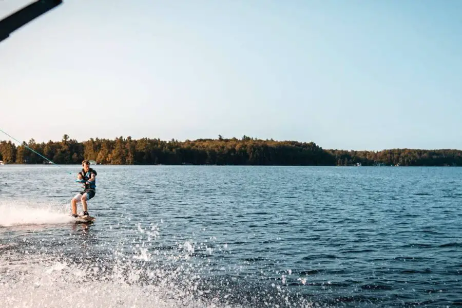 A person wakeboarding on a lake, towed by an off-frame boat using one of the best wakeboard ropes, with a forested shoreline in the background.