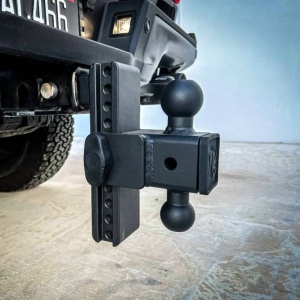 Close-up of a Weigh Safe Steel180 PRO Adjustable Drop Hitch receiver, featuring two hitch balls and a black pin securing the mount. The vehicle's rear tire is partially visible.