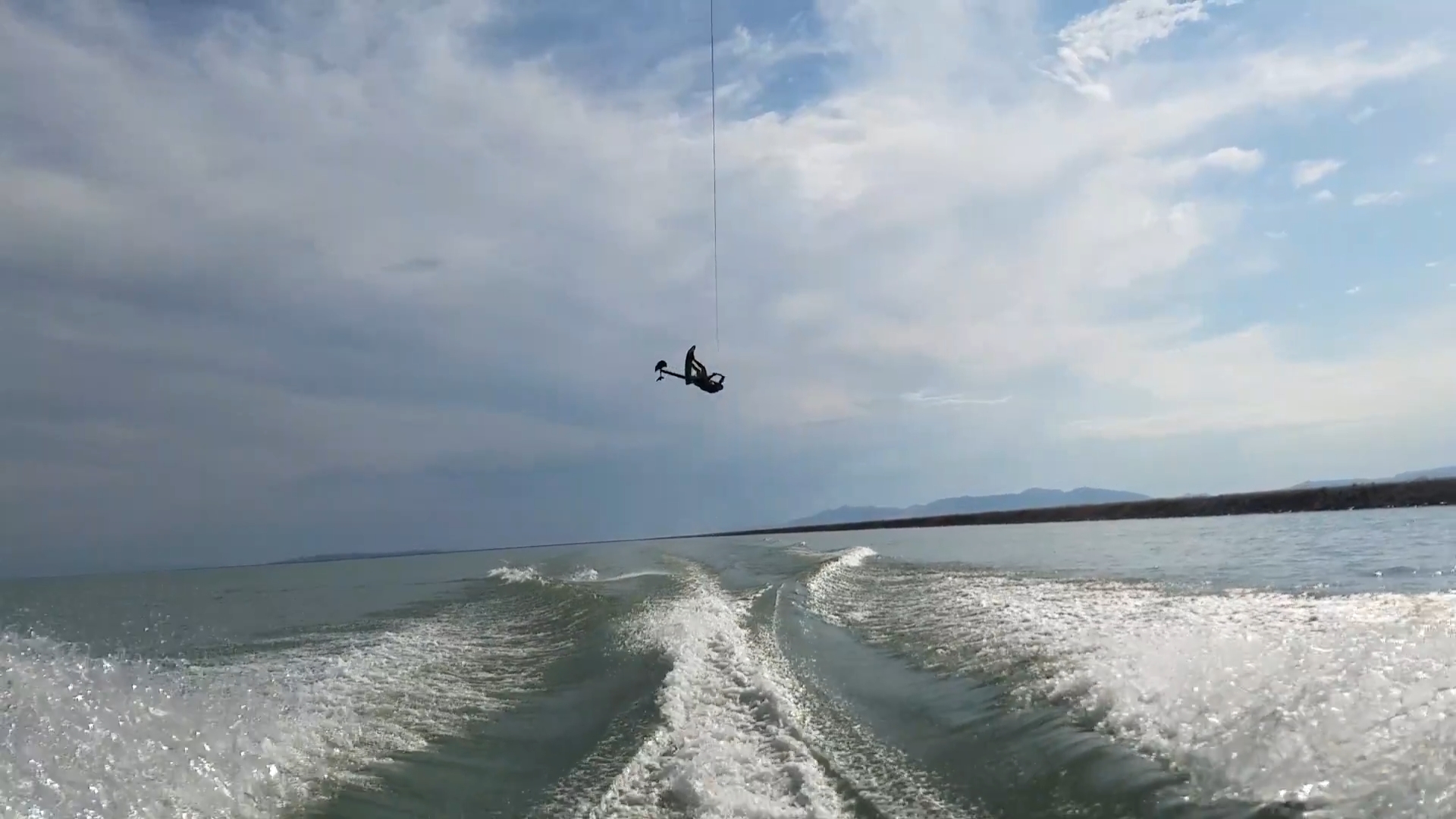 A person is parasailing above the water, trailing behind a speeding boat under a partly cloudy sky, reminiscent of an exhilarating ride on a Sky Ski RS Aero 41 Sit-Down Hydrofoil.