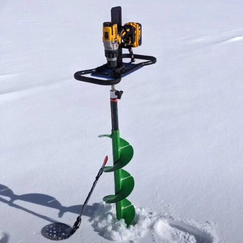 A green ice fishing auger with a yellow and black drill attachment stands upright in the snow, alongside a slotted scoop. This efficient tool can be paired with battery-powered drills for a seamless ice cutting experience.