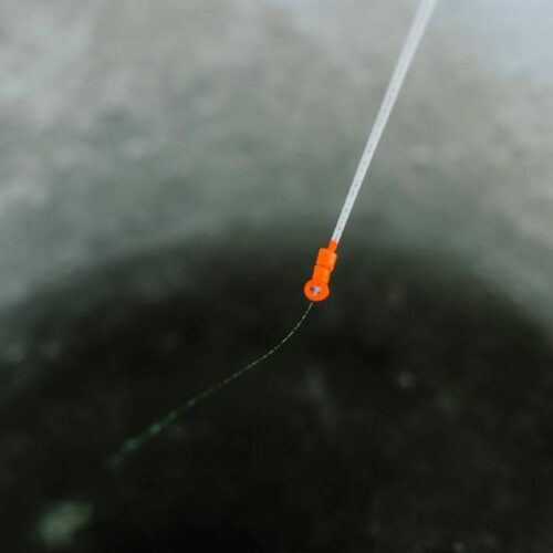 A close-up view of an ice fishing hole with the best ice fishing lines, featuring a fishing line and orange bobber extending into the water.