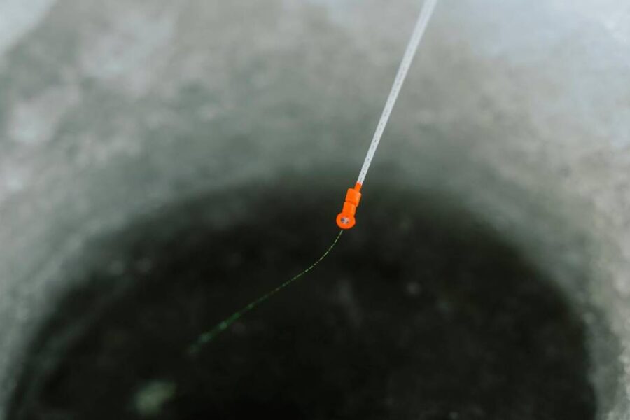 A close-up view of an ice fishing hole with the best ice fishing lines, featuring a fishing line and orange bobber extending into the water.