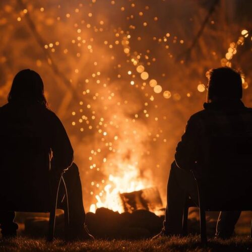 Two people sit in chairs in front of a fire pit at night, surrounded by string lights and a warm glow. The campfire smoke drifts lazily, adding to the atmosphere, as the men and women share stories under the starry sky.