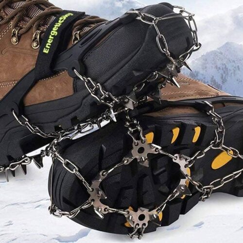 A close-up of boots equipped with metal ice fishing cleats, designed for traction on snowy and icy terrain, with a snowy mountain landscape in the background.