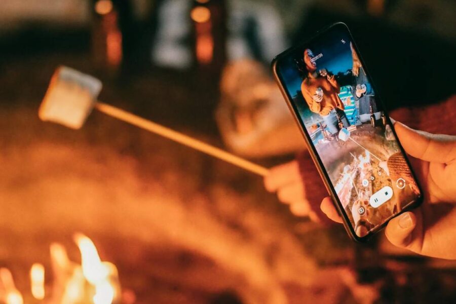 A person holds a smartphone to take a picture of roasting marshmallows over an open fire, mindful of fire pit safety.