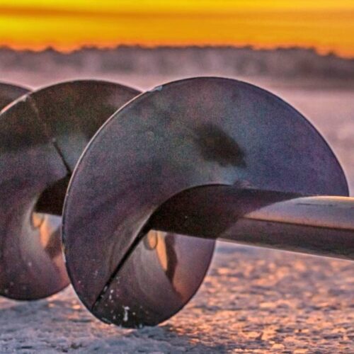 Close-up of an ice auger laying on an icy surface with a gorgeous, vibrant sunset in the background, capturing the essence of ice fishing at lakes in Oregon.