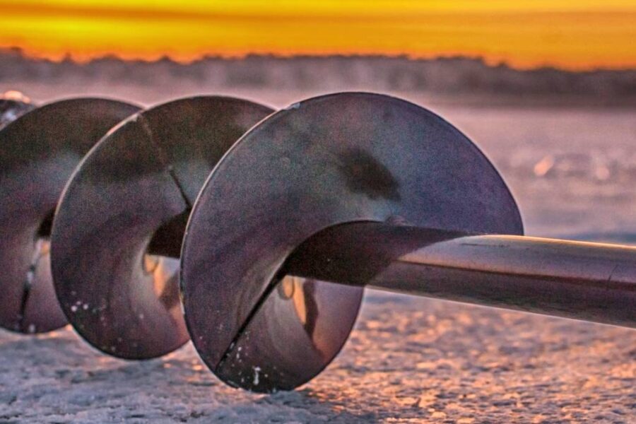 Close-up of an ice auger laying on an icy surface with a gorgeous, vibrant sunset in the background, capturing the essence of ice fishing at lakes in Oregon.