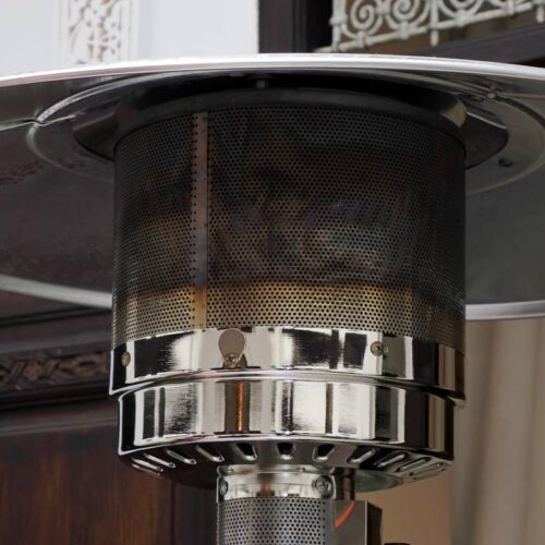 Close-up view of an outdoor patio heater with a metal dome and mesh covering, enhanced by strategic patio heater accessories, positioned in front of a wooden door and draped window.