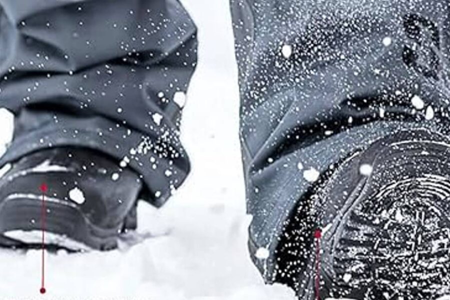 Close-up of a person walking through snow, with visible snowflakes around and snow-covered ice fishing boots. The pants and boots, known for their tread and warmth, appear designed for winter conditions.